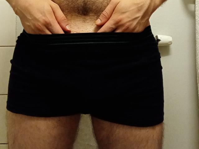 Aure69's hands are pulling down black boxer shorts, exposing a hairy, light-skinned chest and upper thighs. Aure69's penis is not visible.