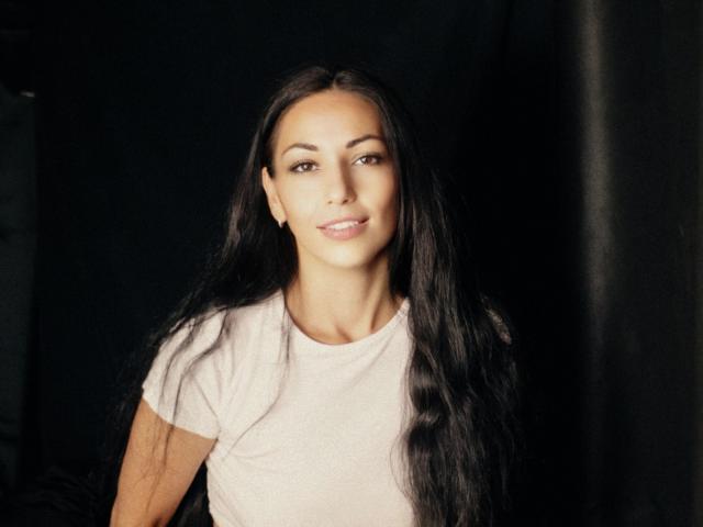 LiluGrants a de longs cheveux noirs, un sourire charmant, et porte une chemise rose pâle. Ses seins sont petits et elle a un visage mince et attrayant..