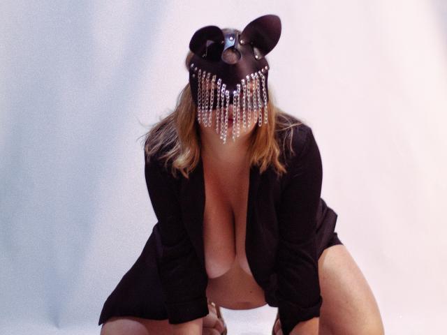 ZannaDreil with mouse mask, hanging beads, black shirt, and exposed tits, kneeling, showing a big ass, blonde hair, and a sexy, mysterious look.