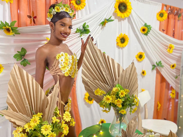 OrianaDollyx holds a paper fan with a red and green pattern, yellow flowers at the bottom. The fan is slightly folded, with the pattern centered. The fan is symmetrical.