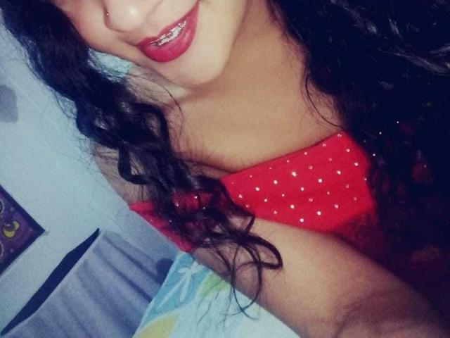 BillyMandy with curly black hair, red polka-dot top, showing her pouty red-lipsticked mouth and small nose ring, focusing on her chest and upper body in a selfie.
