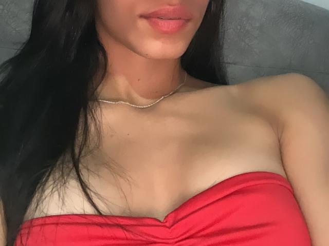 LaurentRay has light skin, black hair, and red strapless top, showing small tits with a slim neck and a thin silver chain. Her lips are slightly pink.