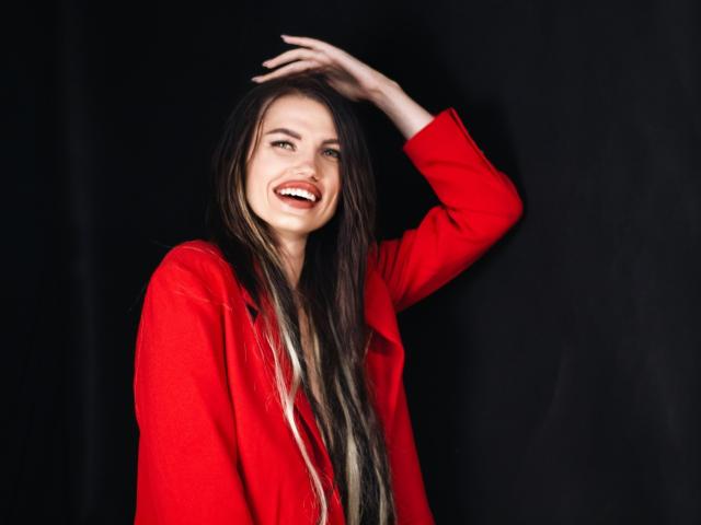 MilaLoona, com pele clara, cabelo escuro, vestindo lingerie de renda preta, expondo os seios, tatuagem no braço esquerdo, mão no cabelo, colar, olhando ligeiramente para o lado, sedutora..