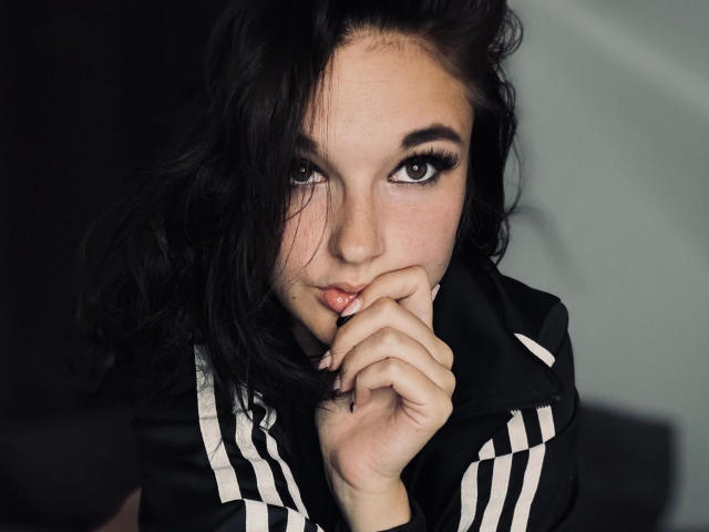 Scarlet-Young-hot with black wavy hair, dark eyes, and full lips, biting her finger, wearing a black and white striped jacket, looking seductively at the camera.