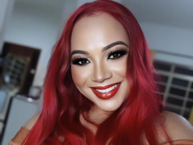 GabAmazing has bright red hair, full eyebrows, long black eyelashes, and red lipstick. She's smiling with shiny white teeth. Her skin is smooth and tan.