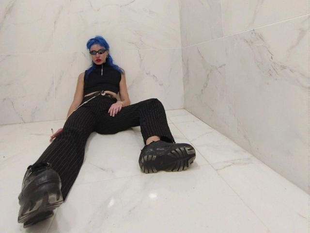 HannaDown-hot with blue hair, black sleeveless top, pinstriped pants, black boots, and glasses, sitting with legs spread, hands on thighs, in a white marble room.