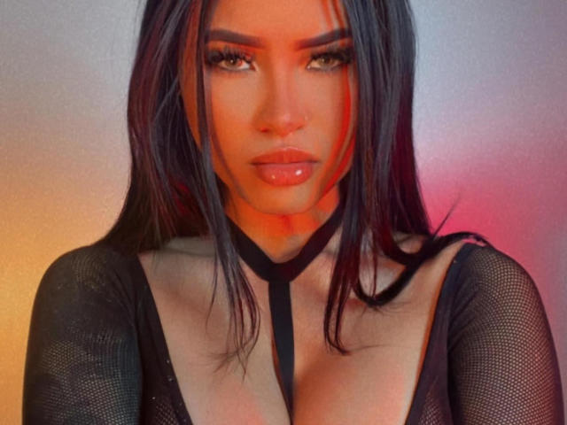 JunneLiu has shiny black hair, thick eyebrows, and glossy lips. She's wearing a black mesh top with a deep neckline, highlighting her big, shiny tits.
