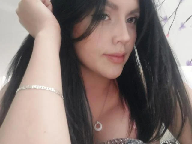 LinaStars with long black hair, hand in hair, wearing a silver bracelet and crescent moon necklace, looking at camera with subtle smile, pink lips, light skin, soft makeup.