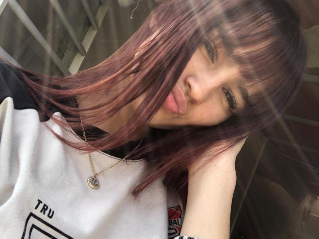 MelodyMansson has light brown skin, straight reddish-brown hair, and is sticking out her tongue. She's wearing a white and black shirt with a small logo, and a necklace.