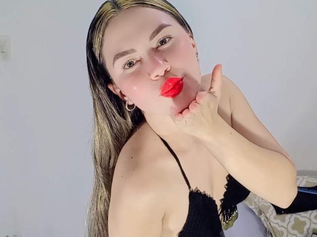 MelParker with blonde and black hair, wearing a black lace bra, kissing her red-lipsticked hand, showing her tits, and a nose ring, with a slightly flushed face.