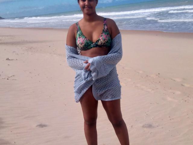 LunaMelynda-hot with brown skin, small tits in a floral bikini, gray knit cardigan, standing on a sandy beach, ocean in background, smiling, holding cardigan open.