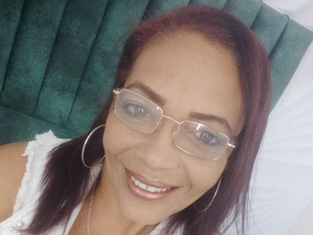 ZoeGreyX with glasses, smiling, wearing a white top, large hoop earrings, and red hair, showing her cute face and pretty blue eyes.