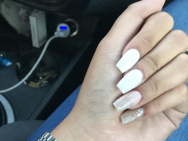 AlexaLip's hand with white, glossy nails and a glittery pink nail on the index finger, showing off her manicure. A silver wristwatch is visible on her wrist.