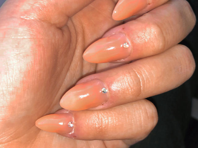 AlexaLip's shiny, nude-painted fingernails with small, sparkly rhinestones on the ring and middle fingers, showing off her glossy, well-manicured hand.
