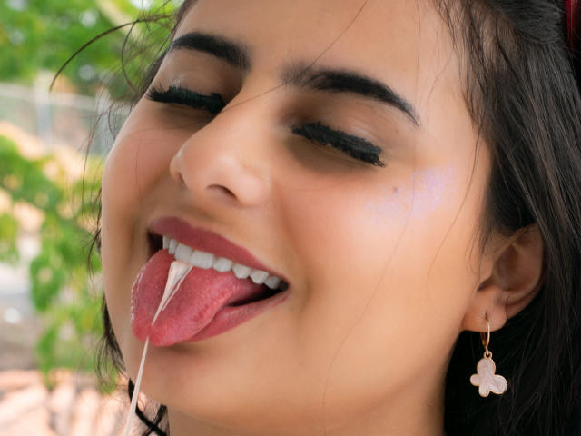 LeilaEvanns has her tongue out with a string of white cum dripping from her mouth. She's wearing pink flower earrings, has black eyeliner, and her eyes are half-closed.