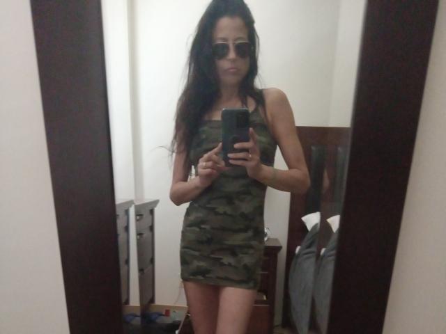 LorenaM with long dark hair, wearing a camo mini-dress, holding a phone, standing in front of a mirror, wearing sunglasses, slim, small tits, small ass.