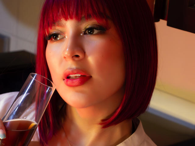 SamanthaEva69 with red bob, holding glass of whiskey, shiny red lips, smoky eye makeup, looking up, soft light on face, white shirt, sexy, sultry expression.