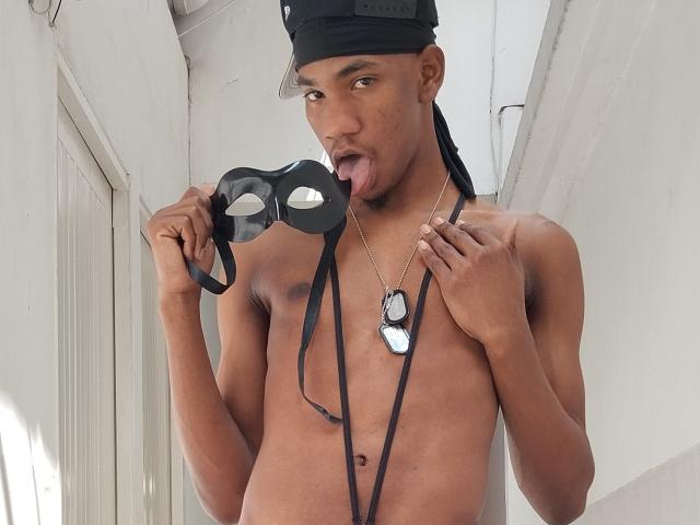 TheCockBoby, shirtless, black mask in hand, tongue out, black cap, dog tags, long black string, dark skin, muscular, looking at camera, standing in white hallway.