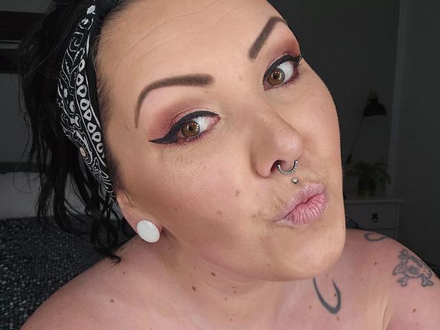 TinyDiamond88 – heiß, mit schwarzen Haaren, einem weißen, gemusterten Stirnband, braunen Augen, auffälligem Eyeliner, einem Nasenring, weißen Ohrringen, vollen Lippen, einem Tattoo an der rechten Schulter und ein paar kleinen Muttermalen..