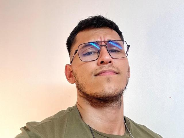 LorenzoReyes with short black hair, glasses, slight beard, green shirt, and a smug, almost confused expression, head tilted back.