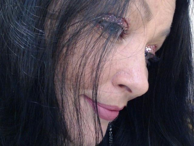 ElaineNights-hot's face with wet black hair covering her eye, pinkish eyeshadow, and pink lipstick. She's looking down with a slight smile, showing her nose and upper lip.