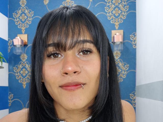 AnnieDarling has dark brown hair, brown eyes, a nose piercing, and a lower lip piercing, with subtle makeup, looking at the camera with a slight smile.
