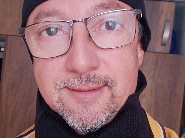 AlexPotter has a goatee, glasses, and a black headscarf, with a slight smile, showing his gray beard and looking directly at the camera.