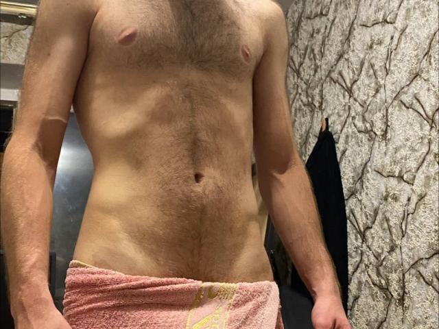 LoveAndSexCouple, shirtless, with a hairy chest, flat stomach, and a pink towel covering their small, flaccid-ass. Their skin is light, and their nipples are small.