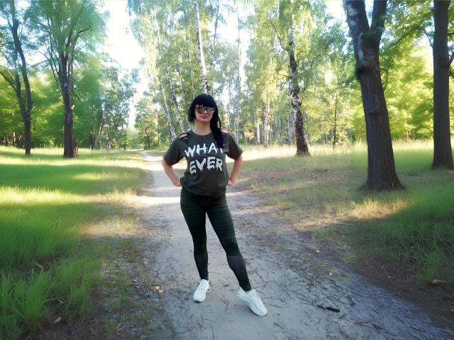 XLylyusX si trova su un sentiero sterrato, indossa una maglietta nera, leggings verdi, scarpe da ginnastica bianche e un berretto nero, con le mani sui fianchi, in una foresta illuminata dal sole..