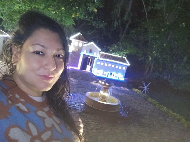 SakotoDika with dark hair, light skin, and a patterned shirt, standing in front of a glowing blue and white house at night, with a lantern on a cobblestone path.