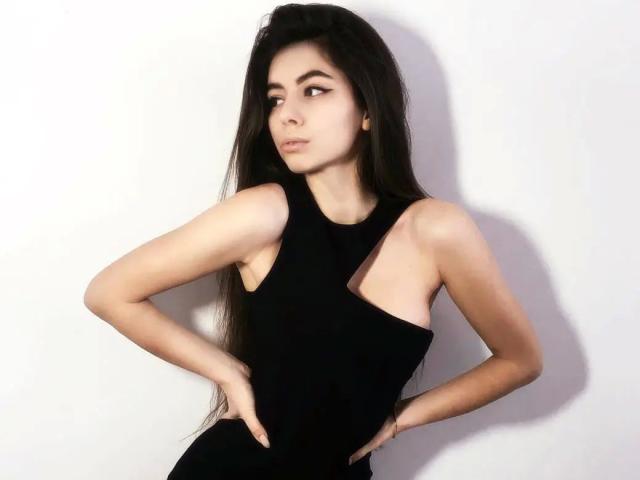 SensualMary-hot with long black hair, wearing a sleeveless black dress, hands on hips, looking to the side, pale skin, small tits, slim build, subtle makeup, white background.