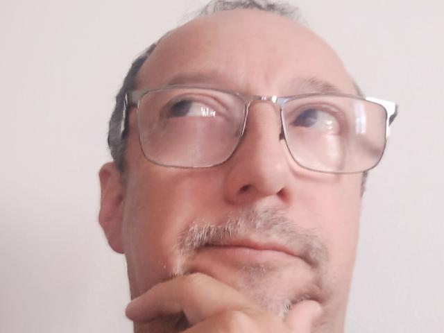 AlexPotter has a bald head with gray hair, glasses, and a mustache, looking up with a serious expression, resting his chin on his hand.