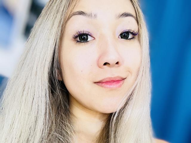 RenyLime has blonde hair, green eyes, pink eyeshadow, long eyelashes, light pink lipstick, and a slight smile. She's staring directly at the camera with a cute face.