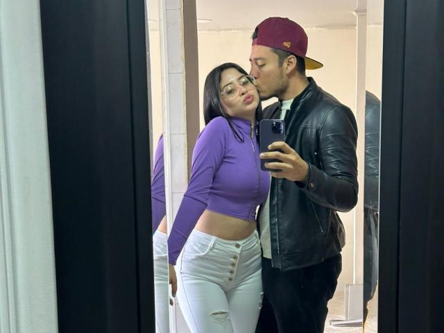 LucyAndJake with small tits, wearing glasses, purple top, white pants, kissing Jake in a black leather jacket, red cap, taking a mirror selfie. Jake holds the phone.