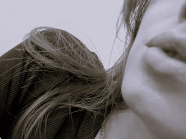 KiraFendy's face, shown in a partial close-up, with her lips slightly parted and long, wavy hair falling across her cheek and over her shoulder. She's wearing a dark, ribbed top.