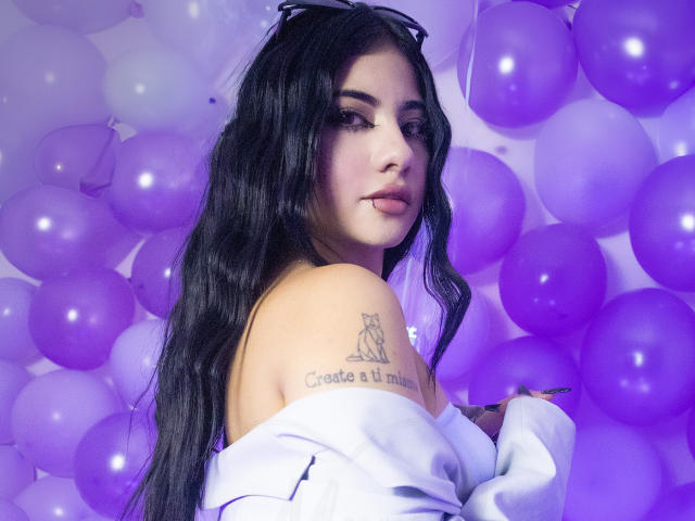 NatallieBlue with long black hair, purple balloons, white off-shoulder shirt, tattoo on left shoulder, looking over shoulder, full lips, slightly parted, sunglasses on head.