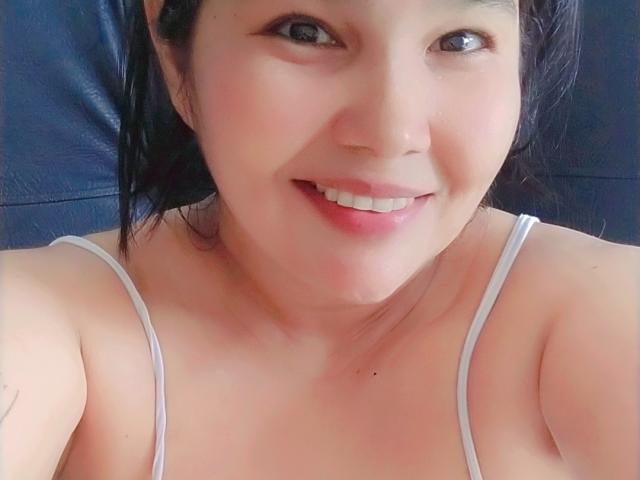 PrittyAlicia has light skin, dark hair, and a cute smile showing her white teeth. She's wearing a white spaghetti strap top, exposing her small, round tits.