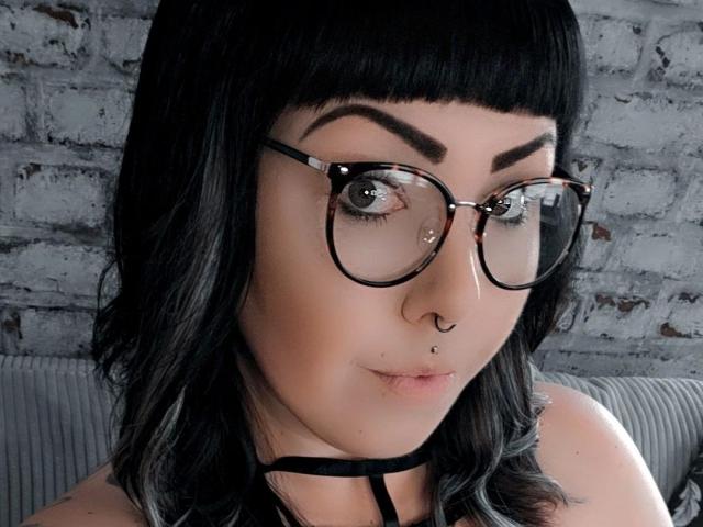 TinyDiamond88-hot heeft zwarte brillen, een zwart, recht bob kapsel, een neusring, een septum piercing en een lichte frons. Haar zwarte haar is schouderlang en ze draagt een zwarte choker..