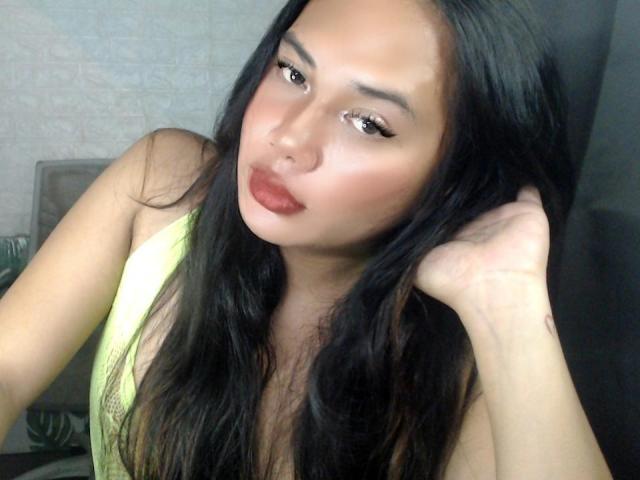 CindyHarper with long black hair, wearing a yellow top, has pouty red lips, and is touching her head with her right hand, looking seductive with half-closed eyes.