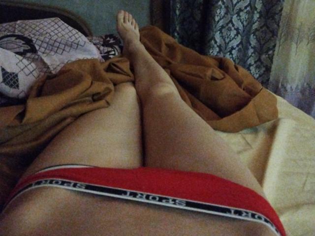 LivvyVictoria's legs are spread, showing her red Victoria's Secret underwear, with her feet pointed upwards, on a bed with brown and patterned blankets.