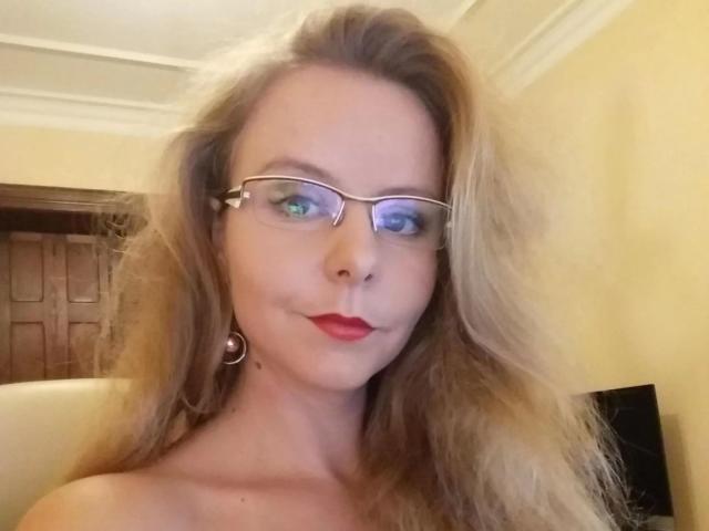 NylonPussy20-hot with long blonde hair, glasses, red lipstick, and hoop earrings, showing off her tits in a selfie. Her ass is not visible.