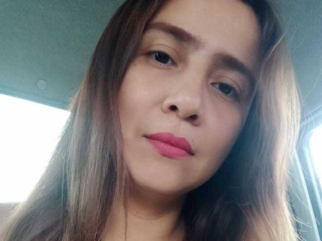 Heidy Wells ha il rossetto rosa, gli occhi marroni e i capelli lunghi castani, con un'espressione leggermente seria, ed è seduta in un'auto. Il suo viso è al centro dell'immagine..