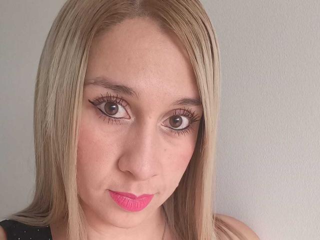 Dana69s has blonde hair, brown eyes, thick black eyeliner, pink lipstick, and a fair skin tone. Her face is centered, looking slightly to the left.