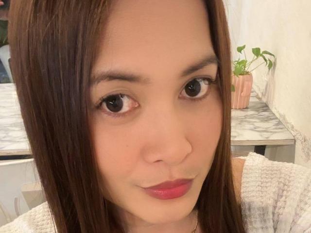 TsAmandaWildSex has brown hair, big brown eyes, pink lips, and a cute face with a subtle smile. She's wearing a white, textured top. Her ass is not visible.
