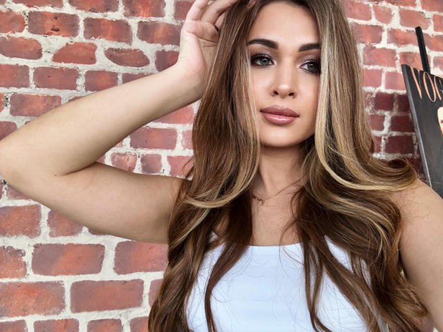 BeataAngel with long brown hair, white tank top, and pink lipstick, hand in hair, looking at camera, showing off her cute tits and sexy ass.