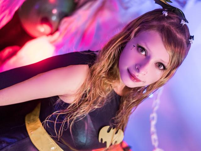 KeiliSexy has wavy blonde hair, a black Batman costume with a gold belt, and bat wings in her hair, with cute black dots on her cheek, looking sexy.