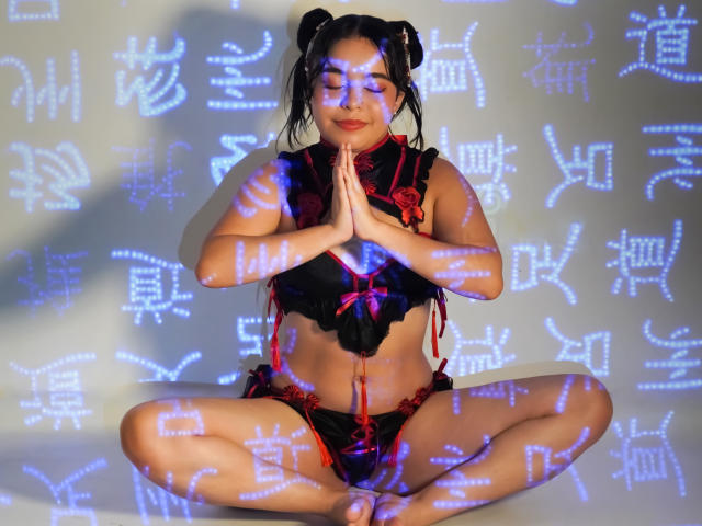 LissyCarter, Asian woman with black double buns, wearing black and red lingerie, sits cross-legged, hands in prayer, illuminated by blue Chinese characters, soft smile, medium tits, slim.