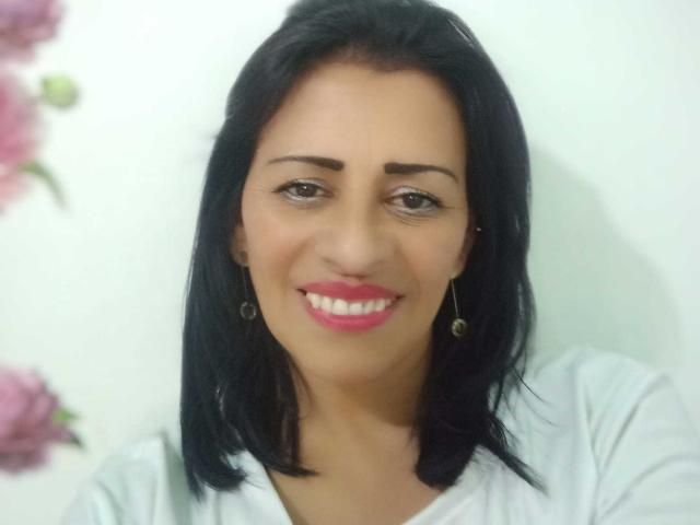 SashaMissHot with black hair, pink lipstick, white shirt, smiling, and earrings, showing off her cute ass and tits in a headshot.