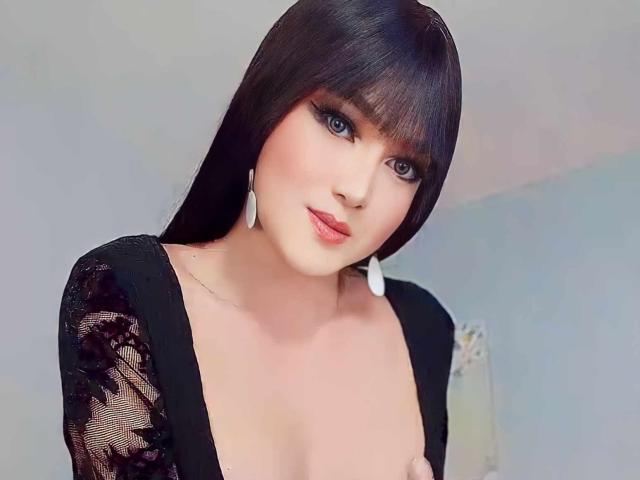 SexyTemptacious with black lace dress, blue eyes, and full pink lips, showing small tits, wearing white feather earrings, and having long black hair with bangs.