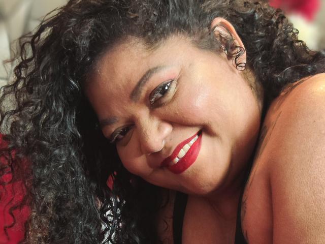 BrunetteBlue with curly black hair, red lipstick, smiling, brown eyes, and nose ring, showing off her smooth, dark brown skin and small, cute nose. Boobs barely visible, topless.